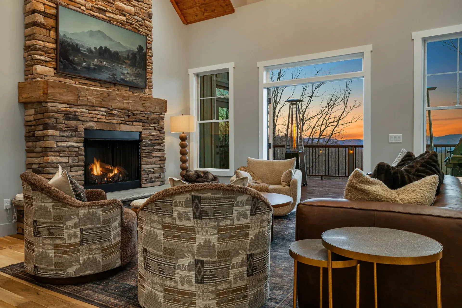 Living room with a stone fireplace and mountain sunset view through floor to ceiling windows