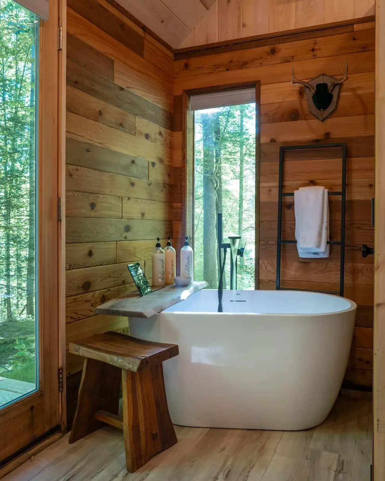 Wood paneled bathroom with a freestanding soaking tub facing a forest view window
