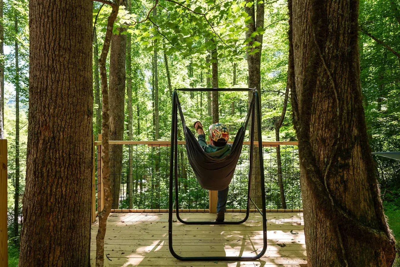 Guest relaxing in a hanging swing chair on a forest deck